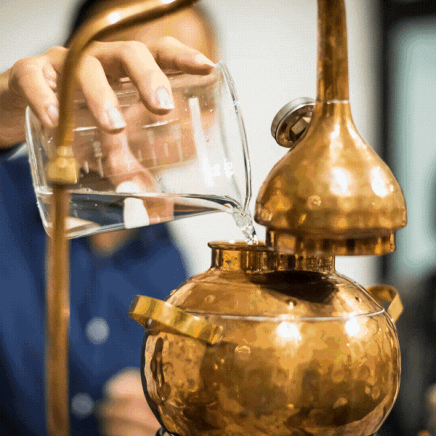 Brass Lion Gin School distillation setup with guest pouring spirit into a mini copper still during a hands-on gin-making experience in Singapore.
